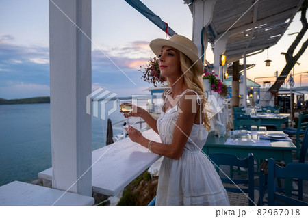 Young woman tourist in straw hat sitting at cliff cafe with sea view at Ermioni, Greece Young woman tourist in straw hat sitting at cliff cafe with sea view at Ermioni, Greece 82967018