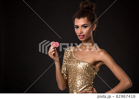 Woman winning - Young woman in a classy gold dress holding two red chips, a poker of aces card combination. 82967416