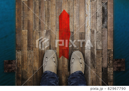 Top view of man standing near the red arrow on old bridge wood floor background. 82967790