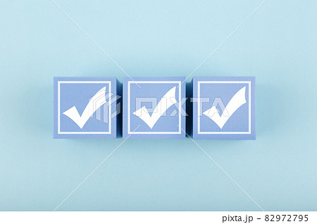 Three white checkmarks on blue cubes against bright pastel blue background  82972795