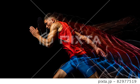 Cropped portrait of young athletic man, professional runner training isolated over black background. Stroboscope effect. 82977519
