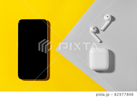 Smartphone and wireless headphones on yellow and gray background. 82977806