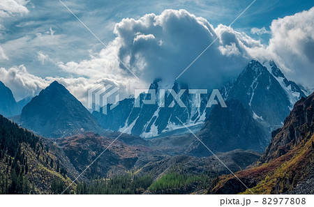 Sharp peaks of the rocks look out from the clouds and morning fog. Wonderful minimalist landscape with big snowy mountain peaks above low clouds. 82977808