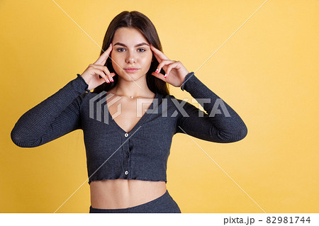 Cropped portrait of young beautiful Caucasian girl touching temples isolated over yellow background Cropped portrait of young beautiful Caucasian girl touching temples isolated over yellow background 82981744