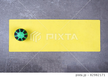 Flat lay of yellow yoga mat with medical ball on concrete floor. Med ball on fitness mat spread out on cement floor 82982171