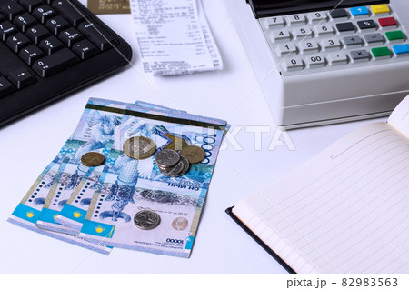 Tenge on a white table with a cash register. Cashier's workplace in Kazakhstan. Salaries in Kazakhstan 82983563