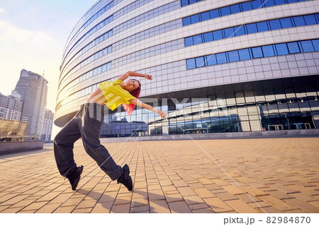 young woman in bright sports clothes and dyed pink hair is dancing in city 82984870