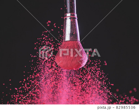 Make-up brush with pink powder explosion on black background 82985536