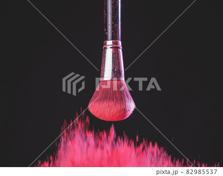 Make-up brush with pink powder explosion on black background 82985537