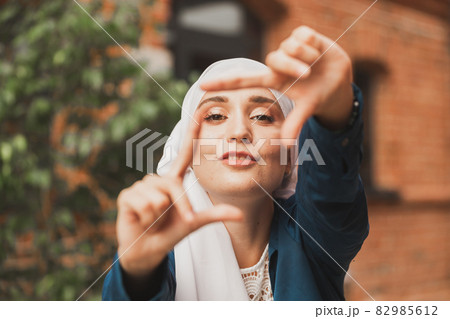 Portrait of young muslim girl making a camera frame with fingers outdoors. 82985612