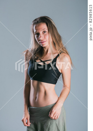 Fitness and diet concept. Portrait of young woman with perfect sporty body and pretty flat abs in sexy sportswear top on gray background. 82985615