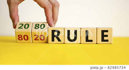 80 on 20 rule symbol. Male hand flips wooden cubes with words '80 on 20 rule'. Beautiful yellow table, white background, copy space. Business and 80 on 20 rule concept. 82985734