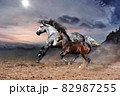 A white horse with a brown foal is galloping rapidly against the backdrop of rocky mountains  82987255