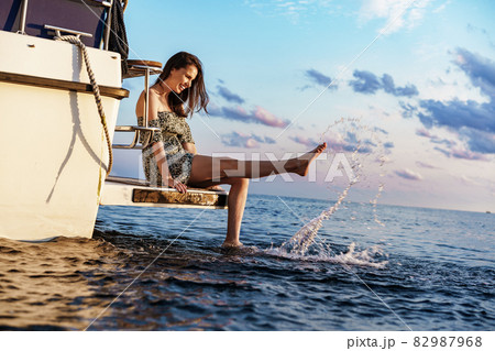 Girl sits on the edge of the yacht with legs splashing in sea water 82987968