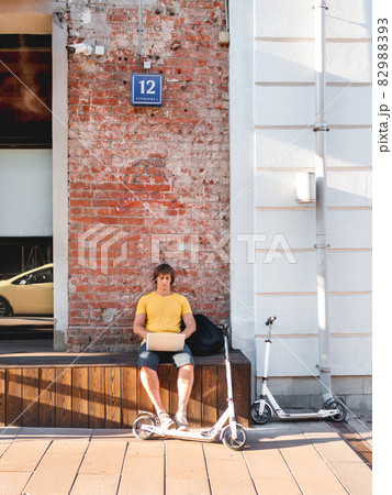 Man sits with laptop on wooden bench in street cafe. Freelancer at work. Student learns remotely from outdoors. Modern lifestyle. Summer vibes. Open air workplace. Man sits with laptop on wooden bench in street cafe. Freelancer at work. Student learns remotely from outdoors. Modern lifestyle. Summer vibes. Open air workplace. 82988393