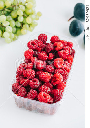 Fresh ripe raspberries in plastic box on white table in kitchen, close-up. Fresh ripe raspberries in plastic box on white table in kitchen, close-up. 82989921