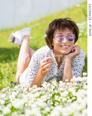 Woman in colorful sunglasses sniffs clover flowers on lawn in urban park. Nature in town. Relax outdoors after work. Summer vibes. 82990293