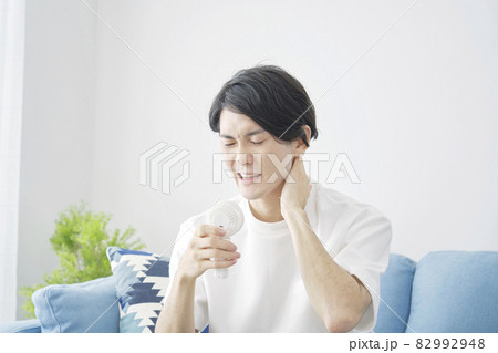 部屋で小型扇風機を使う男性 82992948