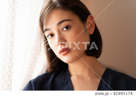 夕暮れの窓辺に立つ女性のポートレート 82995178