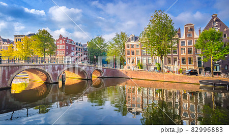 Amsterdam. Panoramic view of the historic city center of Amsterdam. Traditional houses and bridges of Amsterdam. An early quiet morning and the serene reflection of houses in the water. A European Amsterdam. Panoramic view of the historic city center of Amsterdam. Traditional houses and bridges of Amsterdam. An early quiet morning and the serene reflection of houses in the water. A European 82996883