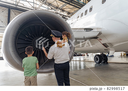 Pilot and children are standing near the turbine and looking at it Pilot and children are standing near the turbine and looking at it 82998517