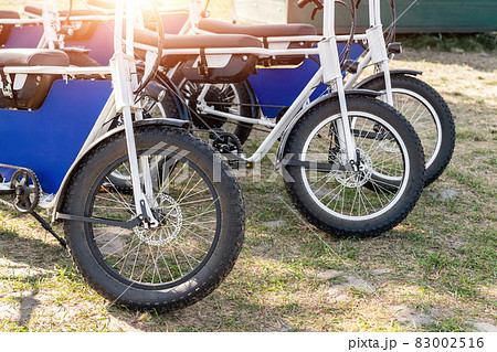 Many retro fat electric bicycle scooters parked on dirt grass field outdoor ready for hire rental sharing cpuntry parl leisure recreation trip. E power transport rent equipment. Rural offroad cycling 83002516