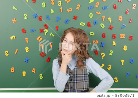 Girl stands in front of a green school board with magnets of numbers that depict her thoughts Girl stands in front of a green school board with magnets of numbers that depict her thoughts 83003971