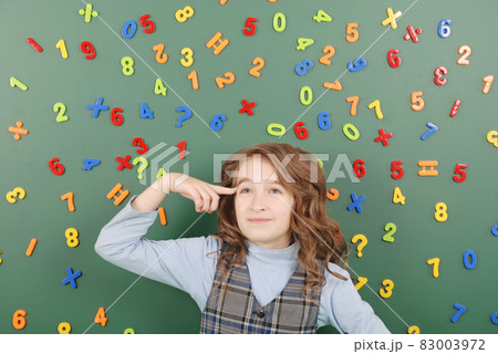 Girl stands in front of a green school board with magnets of numbers that depict her thoughts 83003972