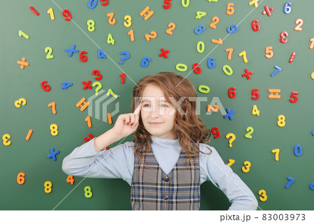 Girl stands in front of a green school board with magnets of numbers that depict her thoughts Girl stands in front of a green school board with magnets of numbers that depict her thoughts 83003973
