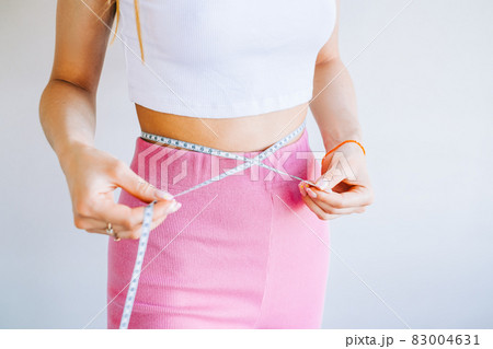Slim woman measuring her waist's size with tape measure on white background. Successful weight loss. Slim fit concept. 83004631