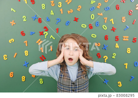 Girl stands in front of a green school board with magnets of numbers that depict her thoughts Girl stands in front of a green school board with magnets of numbers that depict her thoughts 83008295