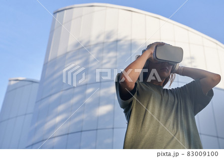 A girl holds virtual reality glasses with her hands, standing against the background of a mirrored building. The concept of the future. High quality photo A girl holds virtual reality glasses with her hands, standing against the background of a mirrored building. The concept of the future. High quality photo 83009100