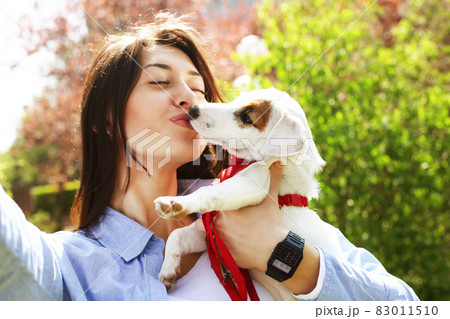 Beautiful young woman in casual outfit on picnic in park with her adorable jack russell terrier puppy, green grass & foliage background. Female owner with small pet, purebred dog. Close up, copy space Beautiful young woman in casual outfit on picnic in park with her adorable jack russell terrier puppy, green grass & foliage background. Female owner with small pet, purebred dog. Close up, copy space 83011510