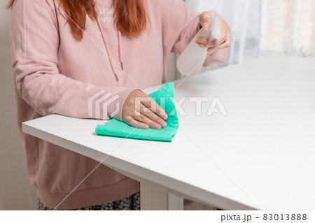 Close up of cleaning white table, sanitizing table surface with disinfectant antibacterial spray bottle, washing surfaces with towel and gloves. COVID-19 prevention sanitizing inside Close up of cleaning white table, sanitizing table surface with disinfectant antibacterial spray bottle, washing surfaces with towel and gloves. COVID-19 prevention sanitizing inside 83013888