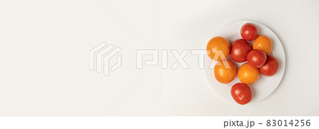 Creative layout made of various fresh red yellow tomato isolated on a white plate on grey background. Top view. Vegan 83014256