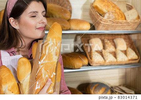 The beautiful saleswoman is delighted with the smell of fresh baguettes. Girl smelling fragrant freshly baked rolls. 83014371