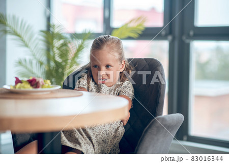A small girl looking unpleased while looking at the food on the table A small girl looking unpleased while looking at the food on the table 83016344