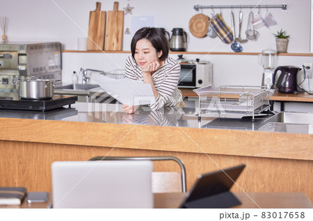 テレワークで席を立ち資料を見る若い女性 83017658