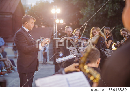 Male conductor directing orchestra performance on the street Male conductor directing orchestra performance on the street 83018389