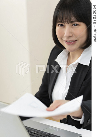 机に座って書類を手渡す若い女性 83020064