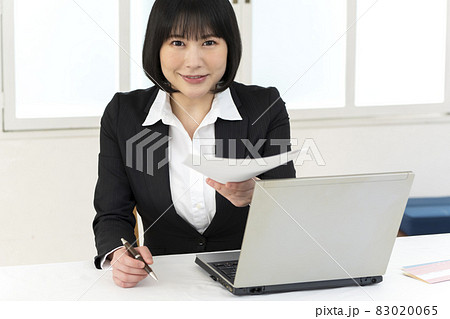 机に座って書類を手渡す若い女性 83020065