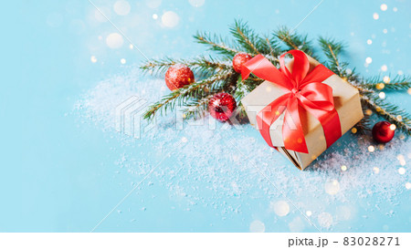 Festive box with a red bow on a blue background with Christmas toys balls branch of fluffy spruce sparkles and confetti . New Year Christmas concept. Flat festive mockup with copy space 83028271