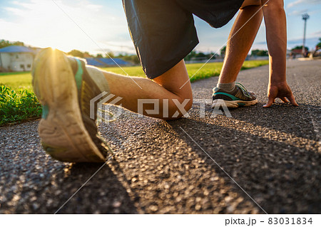 low start for running, close leg view, teen boy runs along the stadium track, a soccer field with green grass - concept of sports and health 83031834