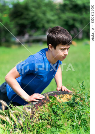 teenage boy exercising outdoors, sports ground in the yard, he does push-ups on the green grass field, healthy lifestyle 83031950