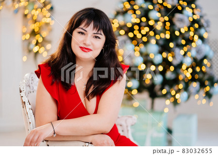 attractive plump woman in red dress against background of Christmas tree 83032655