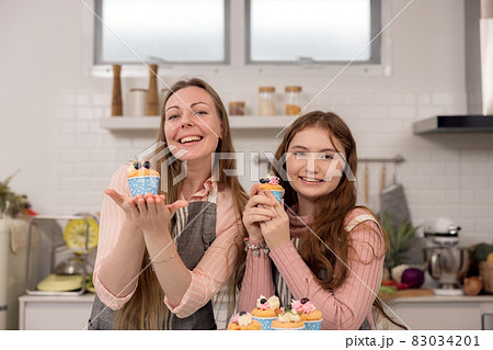 Expectant mother and daughter decorating cupcakes on a kitchen table, having a good time together while eating freshly baked pastries Expectant mother and daughter decorating cupcakes on a kitchen table, having a good time together while eating freshly baked pastries 83034201
