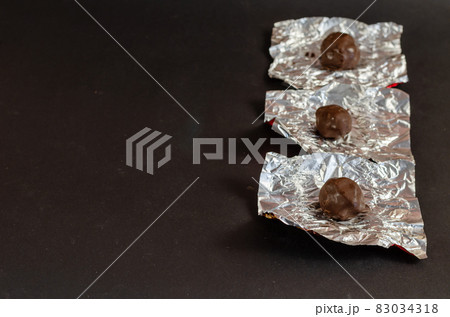 Round chocolates in unwrapped silver wrapper on a black backgrou Round chocolates in unwrapped silver wrapper on a black backgrou 83034318