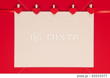 Blank sheet of paper on clothespins with hearts on red background. 83035077
