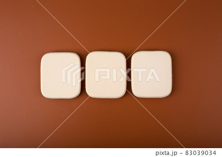 Flat lay with three make up sponges in a row on brown background  83039034