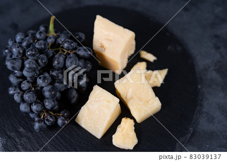 Pieces of aromatic parmesan and black raisins grapes on a dark background. 83039137